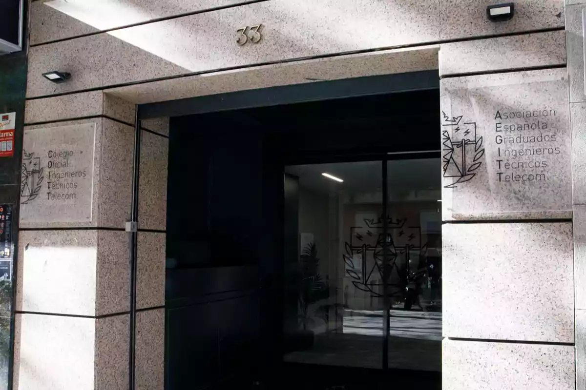 Entrada de un edificio de piedra con el número 33 y placas que indican la sede de asociaciones de ingenieros técnicos de telecomunicaciones