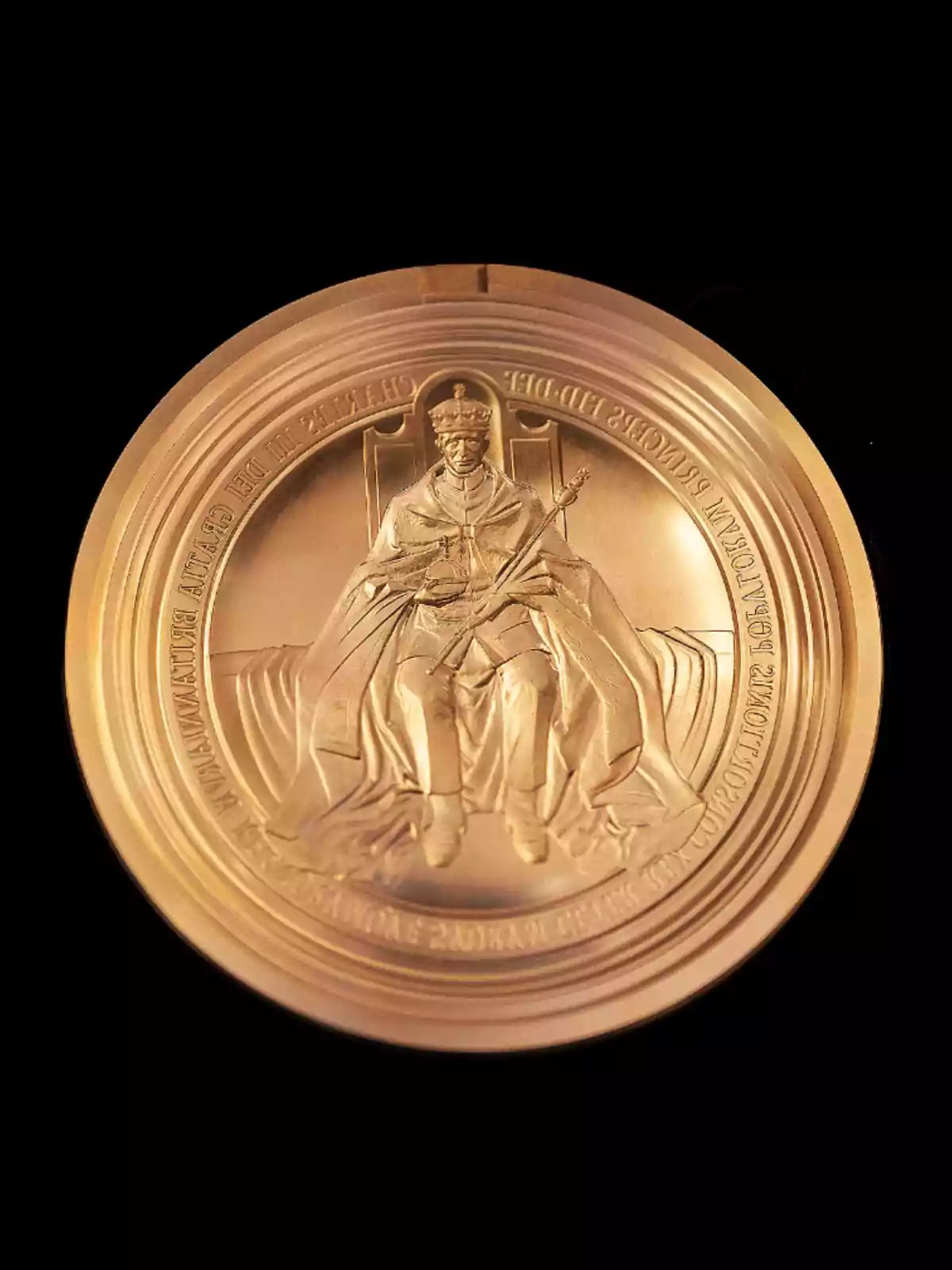 A golden medal with a raised design of a figure seated on a throne holding a scepter, surrounded by inscriptions on the edge. A golden medal with a raised design of a figure seated on a throne holding a scepter, surrounded by inscriptions on the edge.