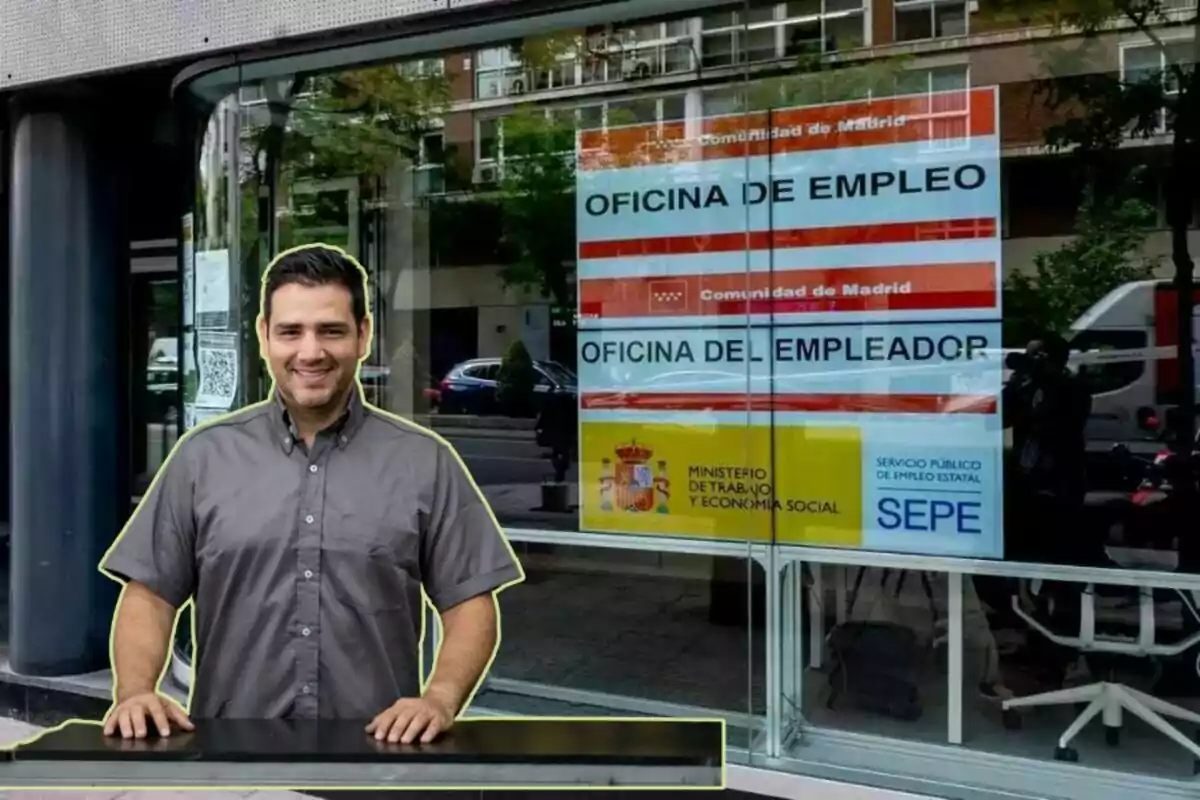 Un hombre sonriente con camisa gris está de pie frente a una oficina de empleo de la Comunidad de Madrid, con un cartel del Ministerio de Trabajo y Economía Social y el SEPE visible en la ventana.