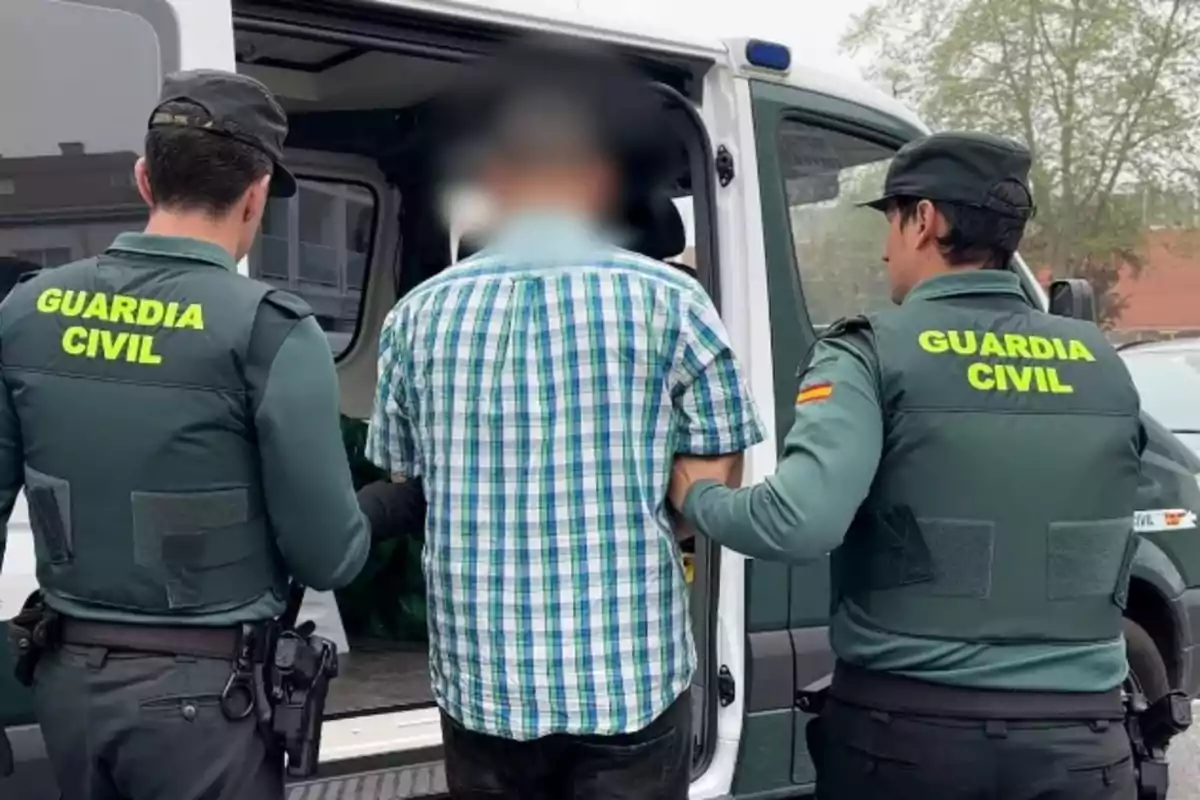 Dos agentes de la Guardia Civil escoltan a un hombre hacia un vehículo oficial.
