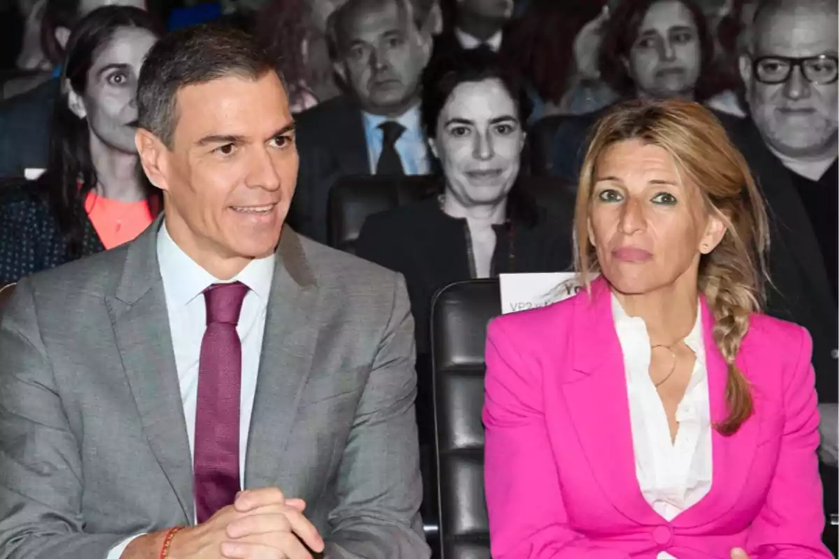 Dos personas sentadas en un evento, una de ellas lleva un traje gris y corbata roja, la otra un traje rosa brillante.