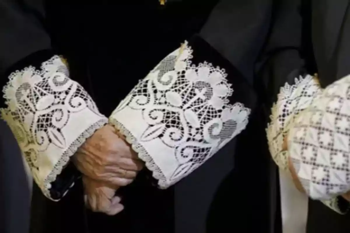 Puños de encaje blanco en la toga de una persona con las manos entrelazadas