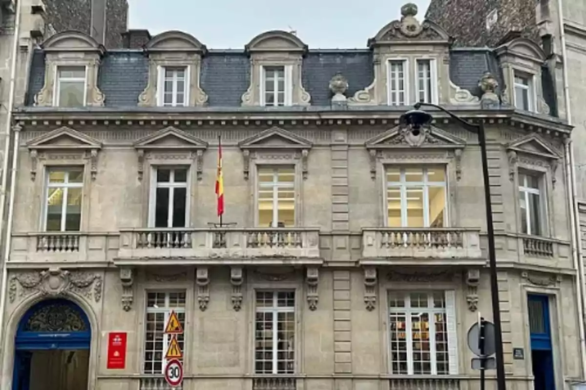 Fachada de un edificio antiguo de piedra con balcones, ventanas grandes y una bandera de España en el centro Fachada de un edificio antiguo de piedra con balcones, ventanas grandes y una bandera de España en el centro