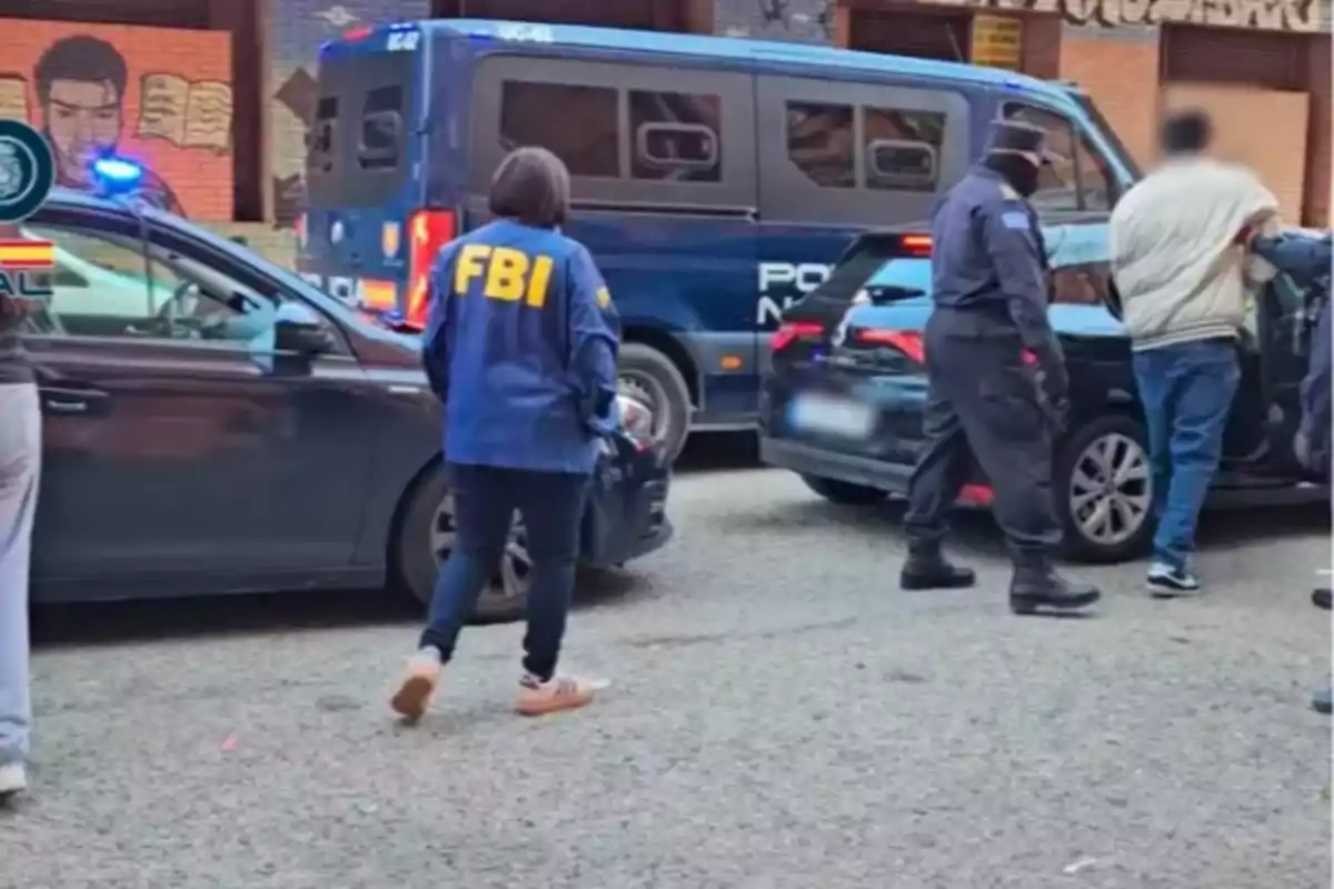 Una agente del FBI y oficiales de policía están en una escena de arresto en la calle junto a varios vehículos policiales. Una agente del FBI y oficiales de policía están en una escena de arresto en la calle junto a varios vehículos policiales.