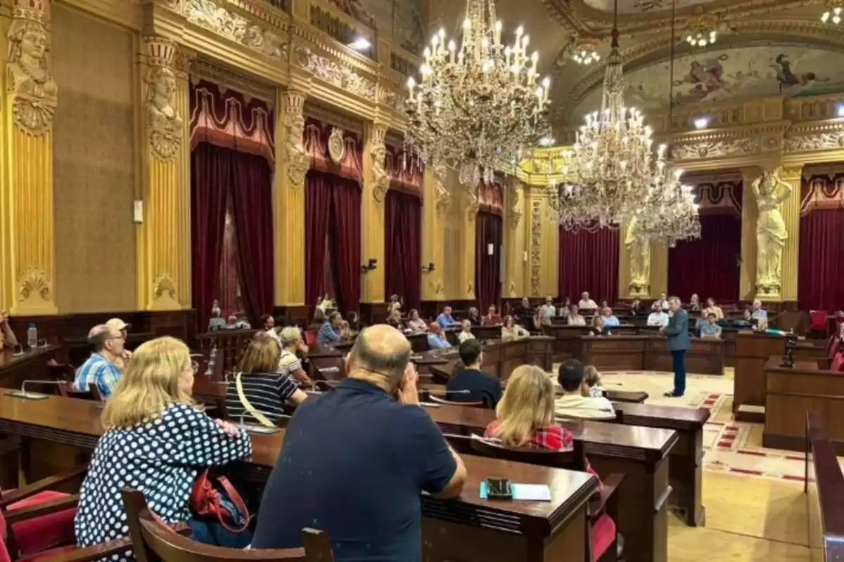 Personas reunidas en una sala de conferencias con decoración elegante y candelabros colgantes.