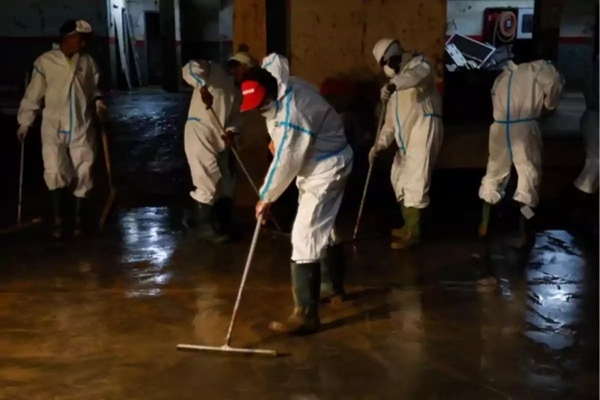 Personas con trajes de protección limpian un área inundada usando escobas y herramientas de limpieza.