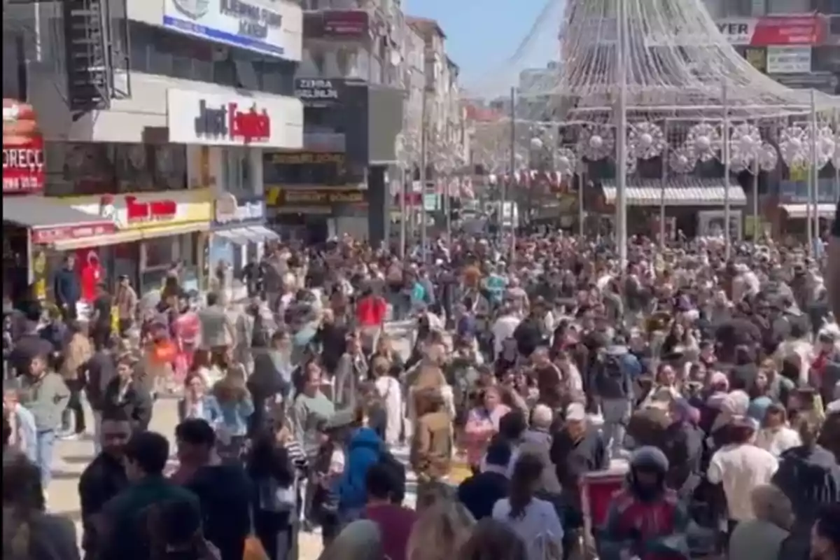 Una multitud de personas camina por una calle concurrida llena de tiendas y decoraciones colgantes.