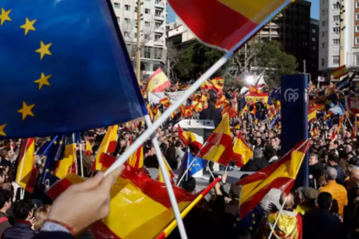 Manifestación multitudinaria en una ciudad con personas ondeando banderas de España y de la Unión Europea