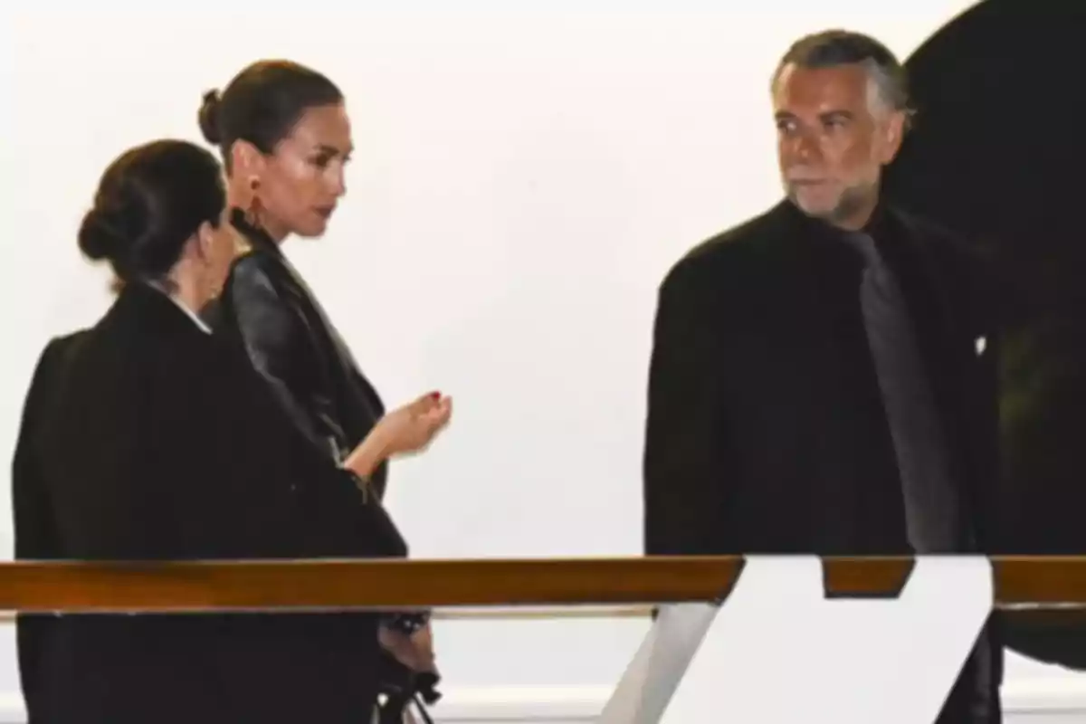 Tres personas vestidas de manera elegante conversan en un entorno iluminado. Tres personas vestidas de manera elegante conversan en un entorno iluminado.