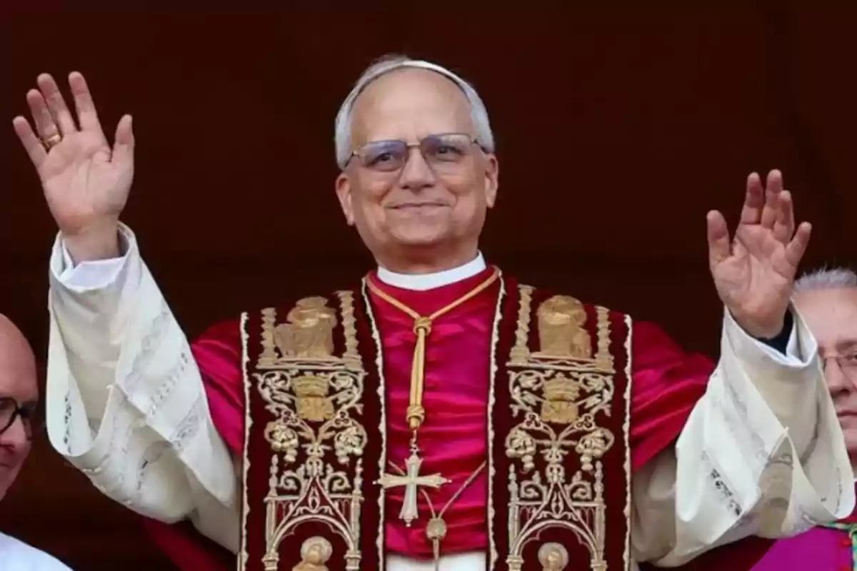 Un hombre con vestimenta religiosa levanta las manos en señal de saludo.