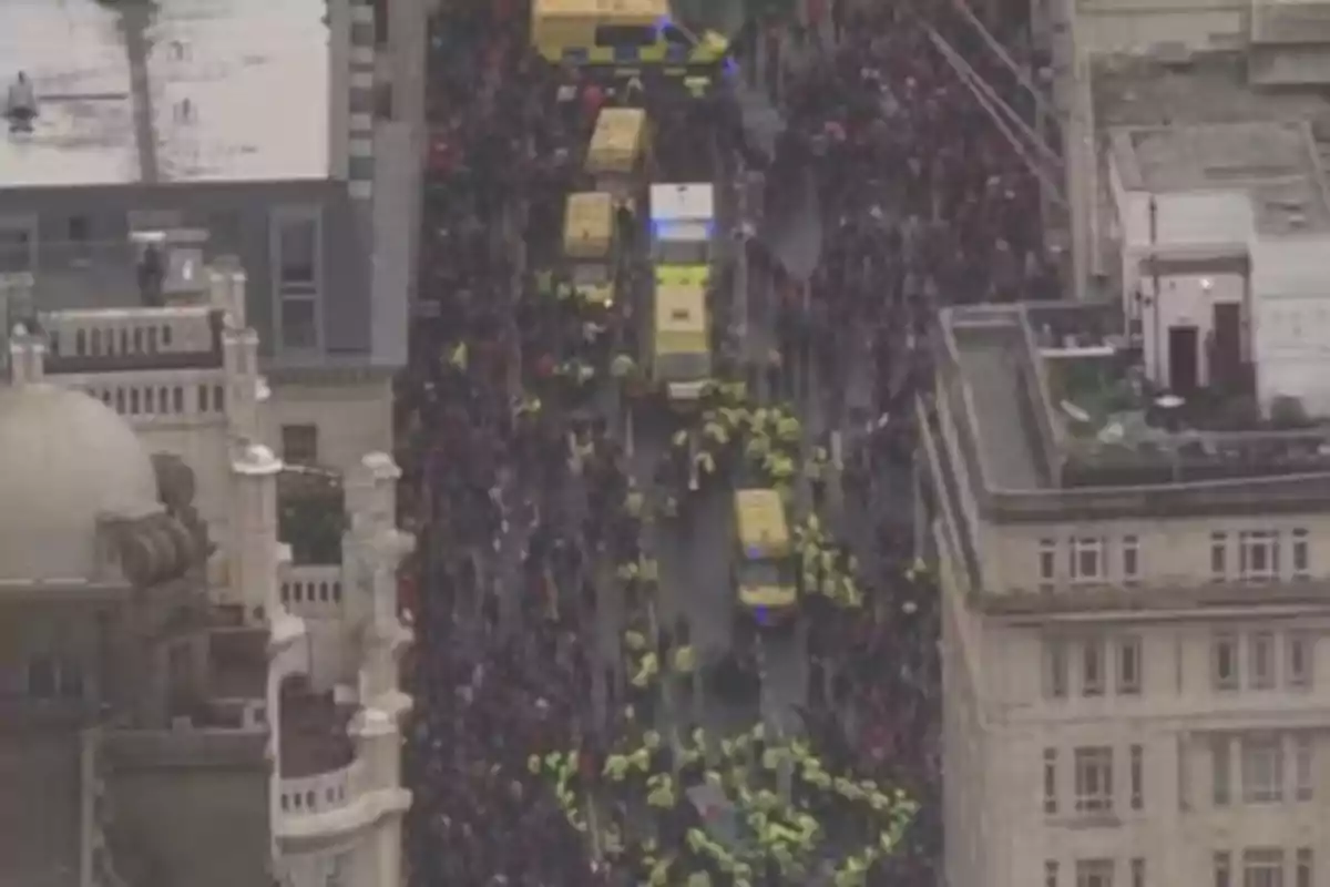 Vista aérea de una multitud en una calle rodeada de edificios con varias ambulancias y personal de seguridad presentes. Vista aérea de una multitud en una calle rodeada de edificios con varias ambulancias y personal de seguridad presentes.