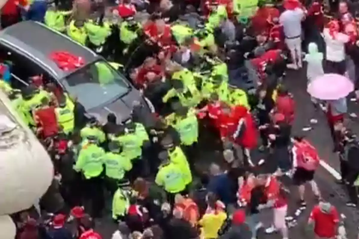 Un coche rodeado de policías y una multitud de personas vestidas de rojo en una calle durante una situación caótica