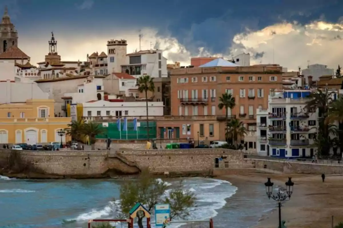 Vista de una ciudad costera con edificios históricos y modernos junto al mar, con un cielo nublado en el fondo.