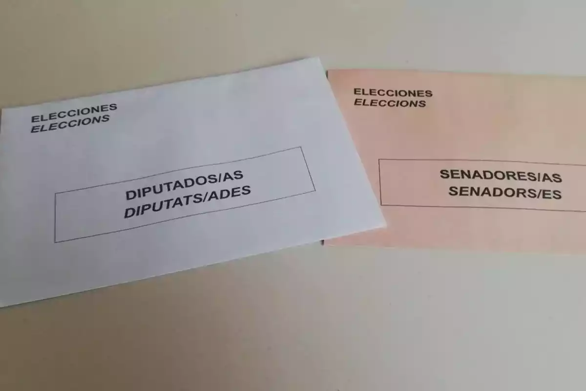 Dos sobres de votación para elecciones, uno blanco para diputaciones y otro color salmón para senadurías, ambos con texto en español y catalán. Dos sobres de votación para elecciones, uno blanco para diputaciones y otro color salmón para senadurías, ambos con texto en español y catalán.