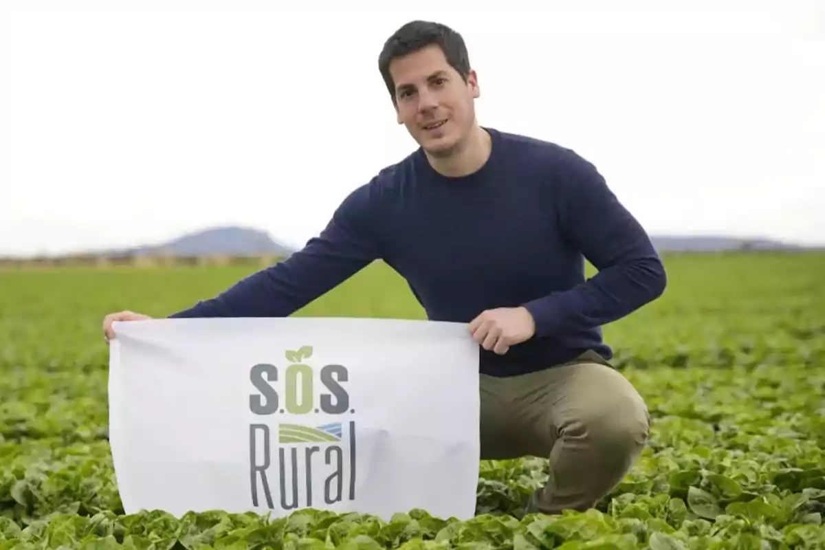 Hombre sosteniendo un cartel de "S.O.S. Rural" en un campo de cultivo.