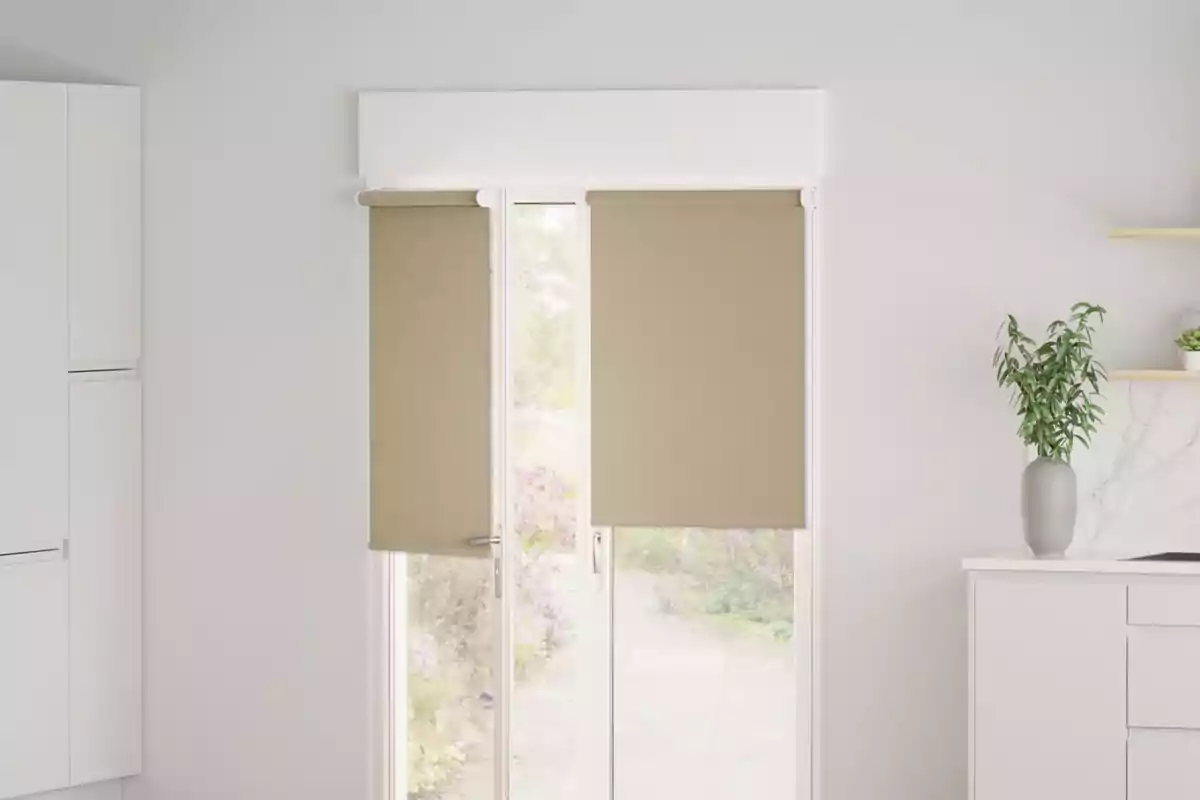 Ventana con persianas enrollables beige en una cocina moderna con una planta en una encimera blanca.