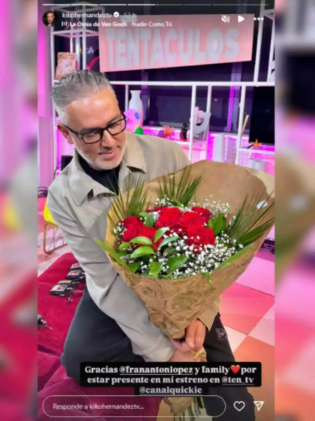 Kiko Hernández sostiene un ramo de flores en un entorno colorido con luces de neón y un cartel que dice Kiko Hernández sostiene un ramo de flores en un entorno colorido con luces de neón y un cartel que dice