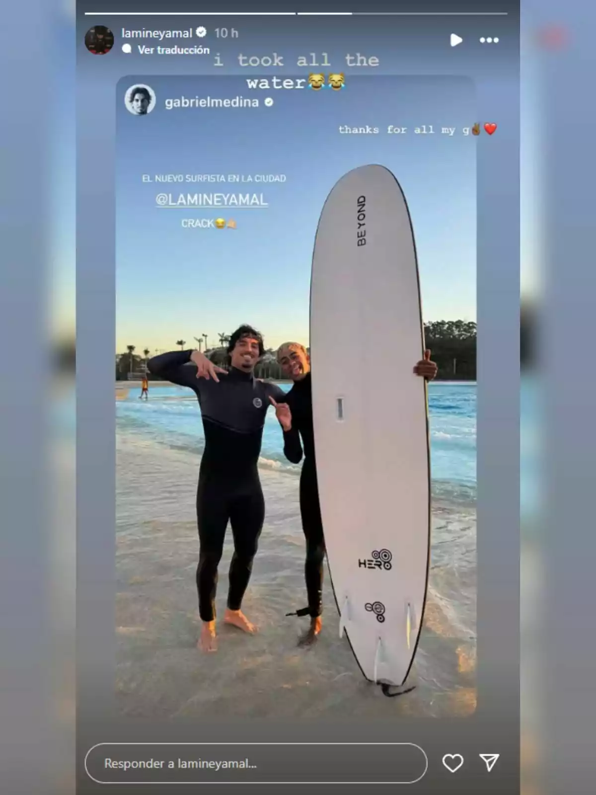 Lamine Yamal and another man in wetsuits pose smiling next to a surfboard on the edge of a wave pool. Lamine Yamal and another man in wetsuits pose smiling next to a surfboard on the edge of a wave pool.