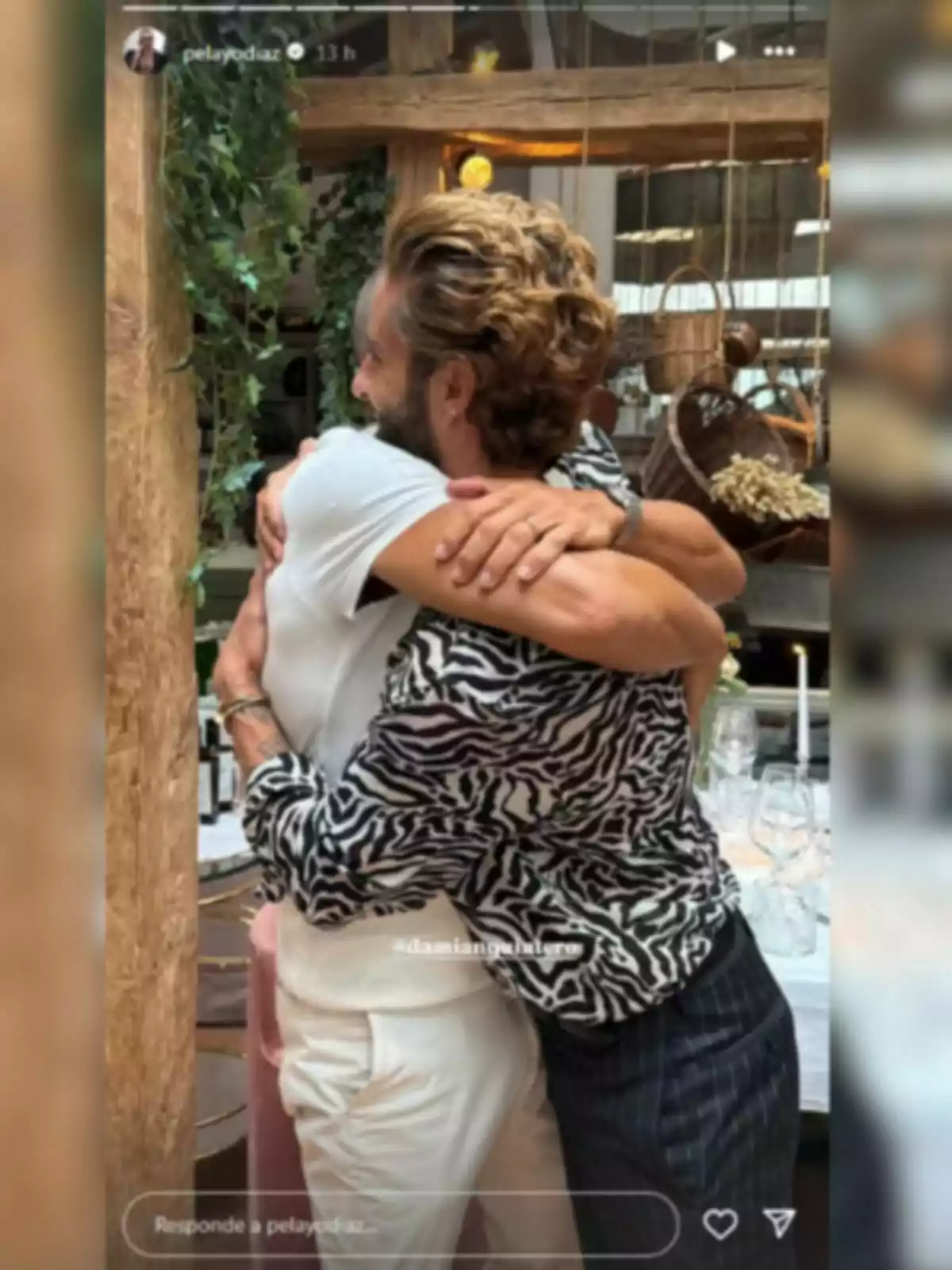 Pelayo Díaz y Damián Quintero abrazándose en un ambiente interior decorado con plantas y mesas puestas Pelayo Díaz y Damián Quintero abrazándose en un ambiente interior decorado con plantas y mesas puestas