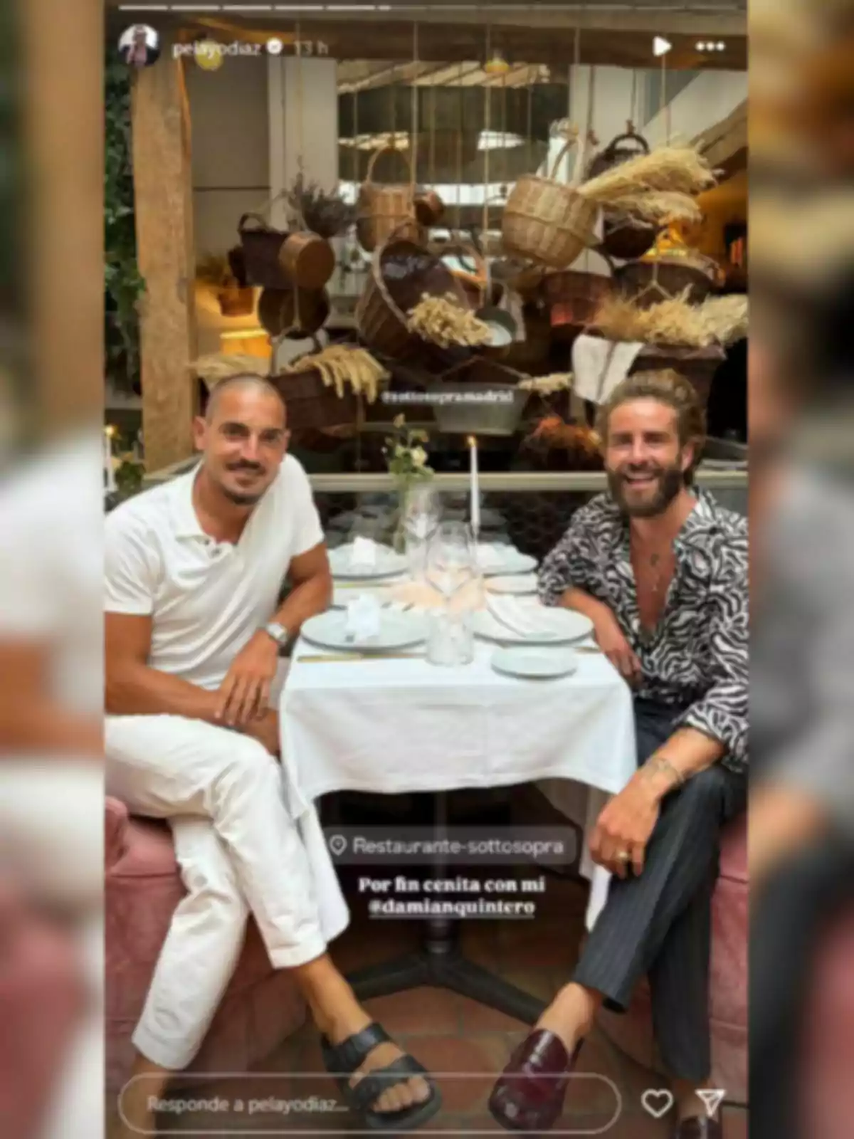 Damián Quintero y Pelayo Díaz sentados en una mesa de restaurante elegantemente decorada, con cestas y plantas colgando de fondo, ambos sonríen y parecen disfrutar de una cena juntos. Damián Quintero y Pelayo Díaz sentados en una mesa de restaurante elegantemente decorada, con cestas y plantas colgando de fondo, ambos sonríen y parecen disfrutar de una cena juntos.