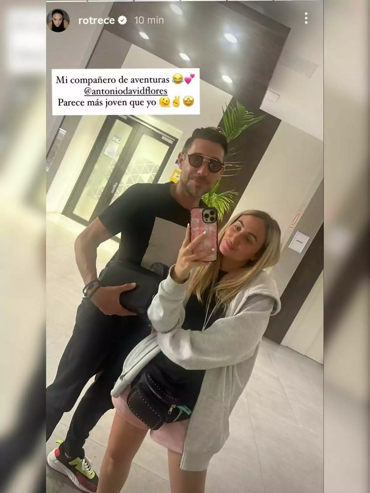 Antonio David y Rocío Flores posan juntas para una selfie en un vestíbulo moderno, una de ellas sostiene el teléfono mientras ambos sonríen y visten ropa casual Antonio David y Rocío Flores posan juntas para una selfie en un vestíbulo moderno, una de ellas sostiene el teléfono mientras ambos sonríen y visten ropa casual