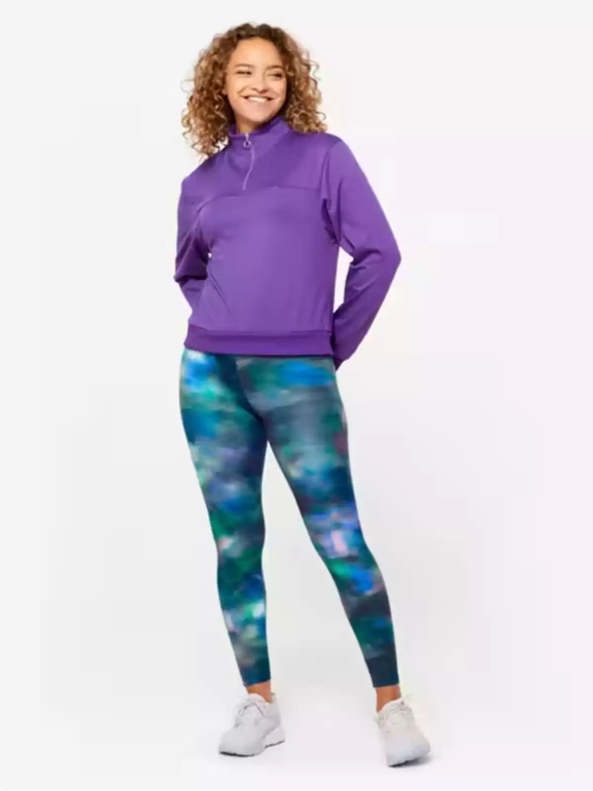 Mujer sonriendo con sudadera morada y leggings con estampado colorido, de pie sobre un fondo claro. Mujer sonriendo con sudadera morada y leggings con estampado colorido, de pie sobre un fondo claro.