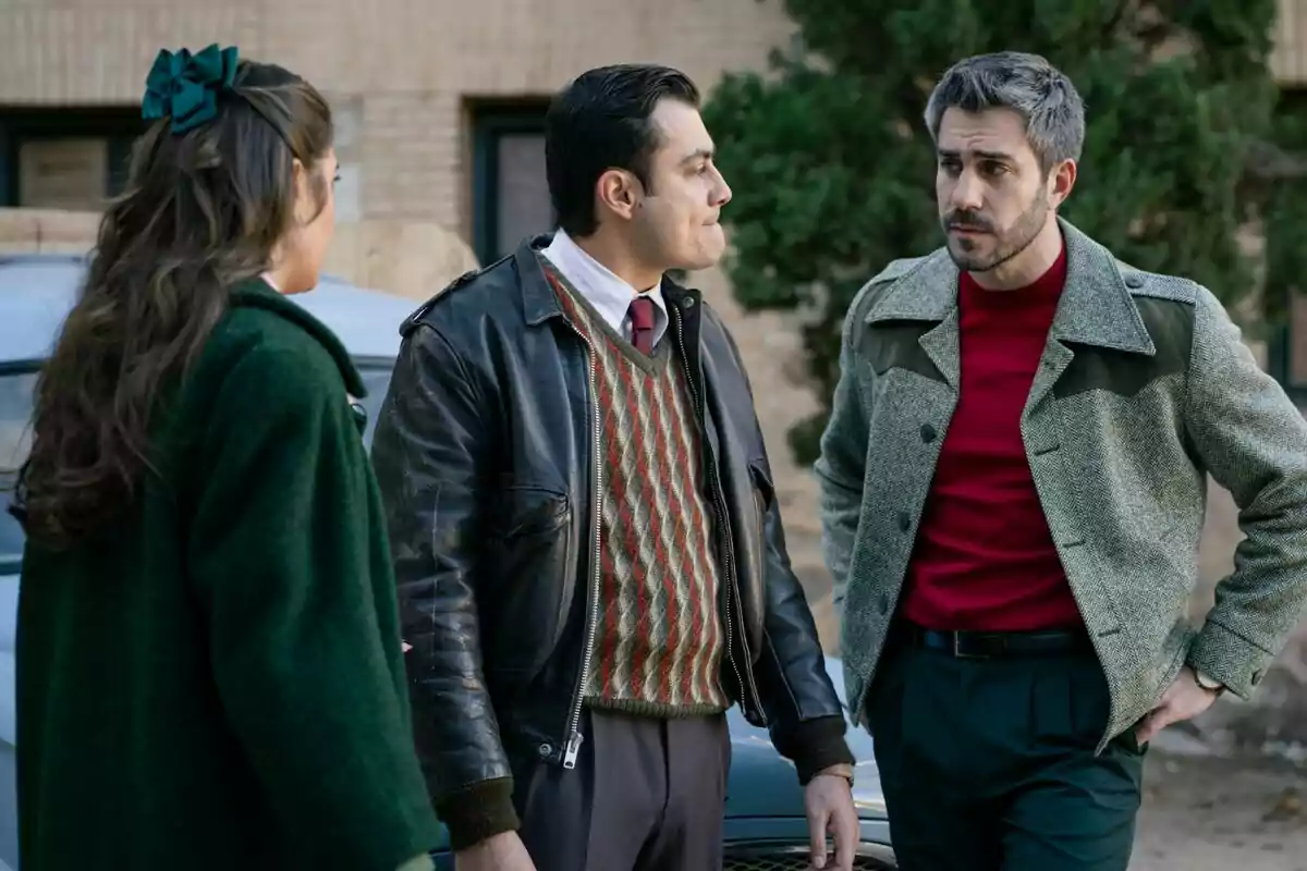 Dani Tatay, José Milán y Alba Brunet conversan al aire libre, dos hombres y una mujer, todos vestidos con ropa de estilo retro, con un coche y un edificio de fondo en Sueños de Libertad. Dani Tatay, José Milán y Alba Brunet conversan al aire libre, dos hombres y una mujer, todos vestidos con ropa de estilo retro, con un coche y un edificio de fondo en Sueños de Libertad.