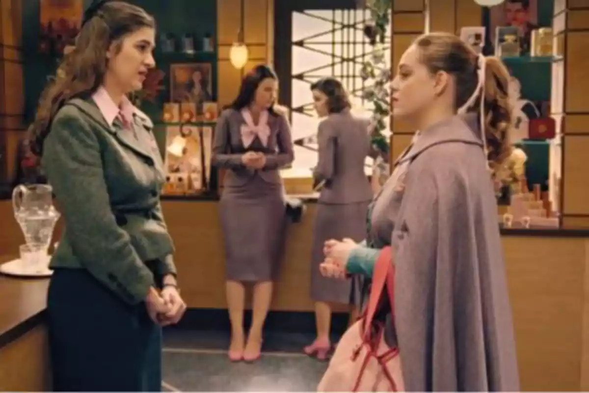 Dos mujeres conversan en una tienda decorada con productos en estantes mientras otras dos mujeres están al fondo junto a una ventana. Captura de 'Sueños de libertad' Dos mujeres conversan en una tienda decorada con productos en estantes mientras otras dos mujeres están al fondo junto a una ventana. Captura de 'Sueños de libertad'