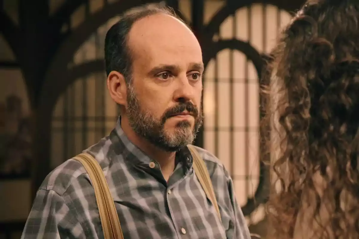 Gaspar con barba y camisa a cuadros mira a otra persona en un entorno interior con ventanas de fondo. Captura de 'Sueños de libertad'