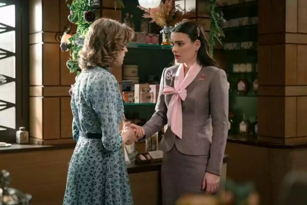 Marta y Fina conversando y estrechándose las manos en una tienda decorada con plantas y productos en estantes. Captura de 'Sueños de libertad'