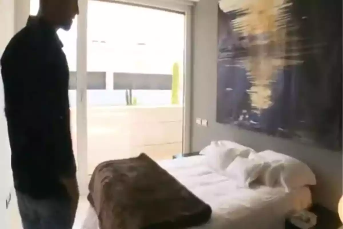 Gonzalo Miró de pie en una habitación moderna con una cama cubierta por una manta marrón y un gran cuadro abstracto en la pared. Captura de 'Supercasas' Gonzalo Miró de pie en una habitación moderna con una cama cubierta por una manta marrón y un gran cuadro abstracto en la pared. Captura de 'Supercasas'