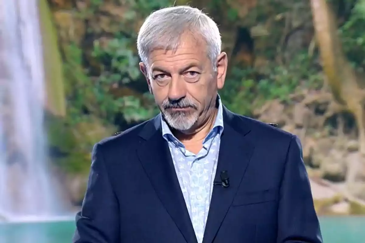 Carlos Sobera, vestido con traje oscuro y camisa clara, está de pie frente a un fondo natural con vegetación y una cascada. Captura de 'Supervivientes' Carlos Sobera, vestido con traje oscuro y camisa clara, está de pie frente a un fondo natural con vegetación y una cascada. Captura de 'Supervivientes'