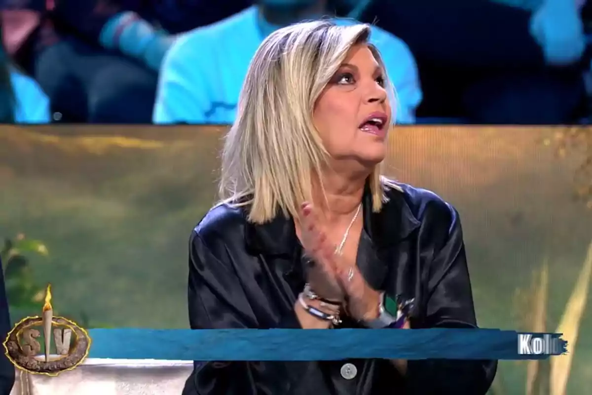 Terelu Campos con chaqueta oscura está sentada en un estudio de televisión, mirando hacia arriba y aplaudiendo, con un público desenfocado al fondo. Captura de 'Supervivientes' Terelu Campos con chaqueta oscura está sentada en un estudio de televisión, mirando hacia arriba y aplaudiendo, con un público desenfocado al fondo. Captura de 'Supervivientes'