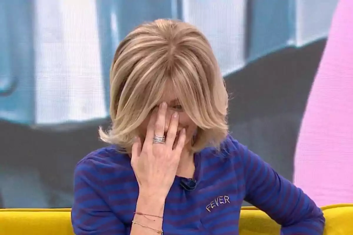 Susanna Griso con cabello rubio se cubre el rostro con la mano mientras está sentada en un sofá amarillo y lleva una camiseta azul con rayas en 'Espejo Público'. Susanna Griso con cabello rubio se cubre el rostro con la mano mientras está sentada en un sofá amarillo y lleva una camiseta azul con rayas en 'Espejo Público'.