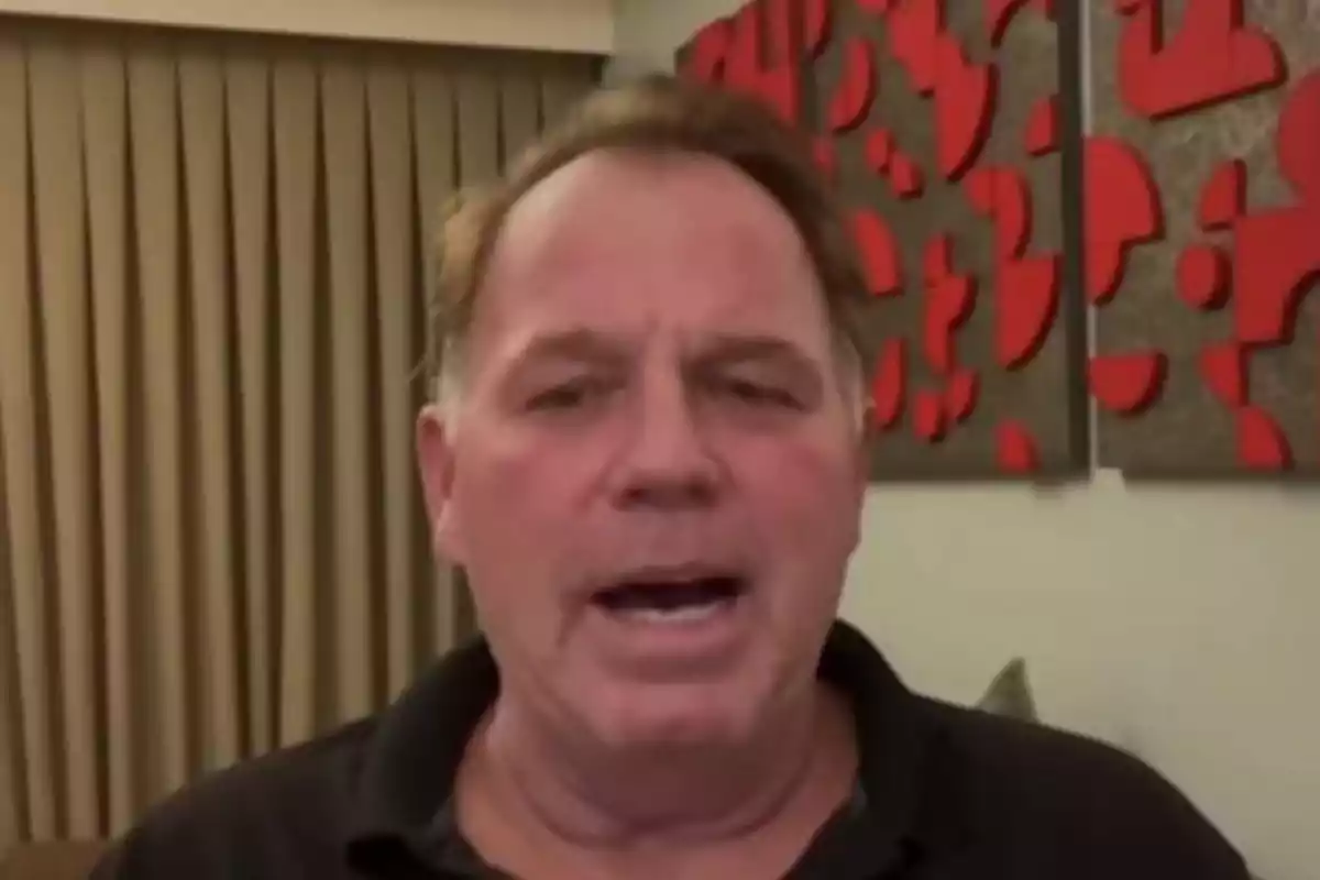 Thomas Markle Jr. con camisa oscura está hablando frente a una cortina beige y una pared decorada con formas geométricas rojas. Thomas Markle Jr. con camisa oscura está hablando frente a una cortina beige y una pared decorada con formas geométricas rojas.