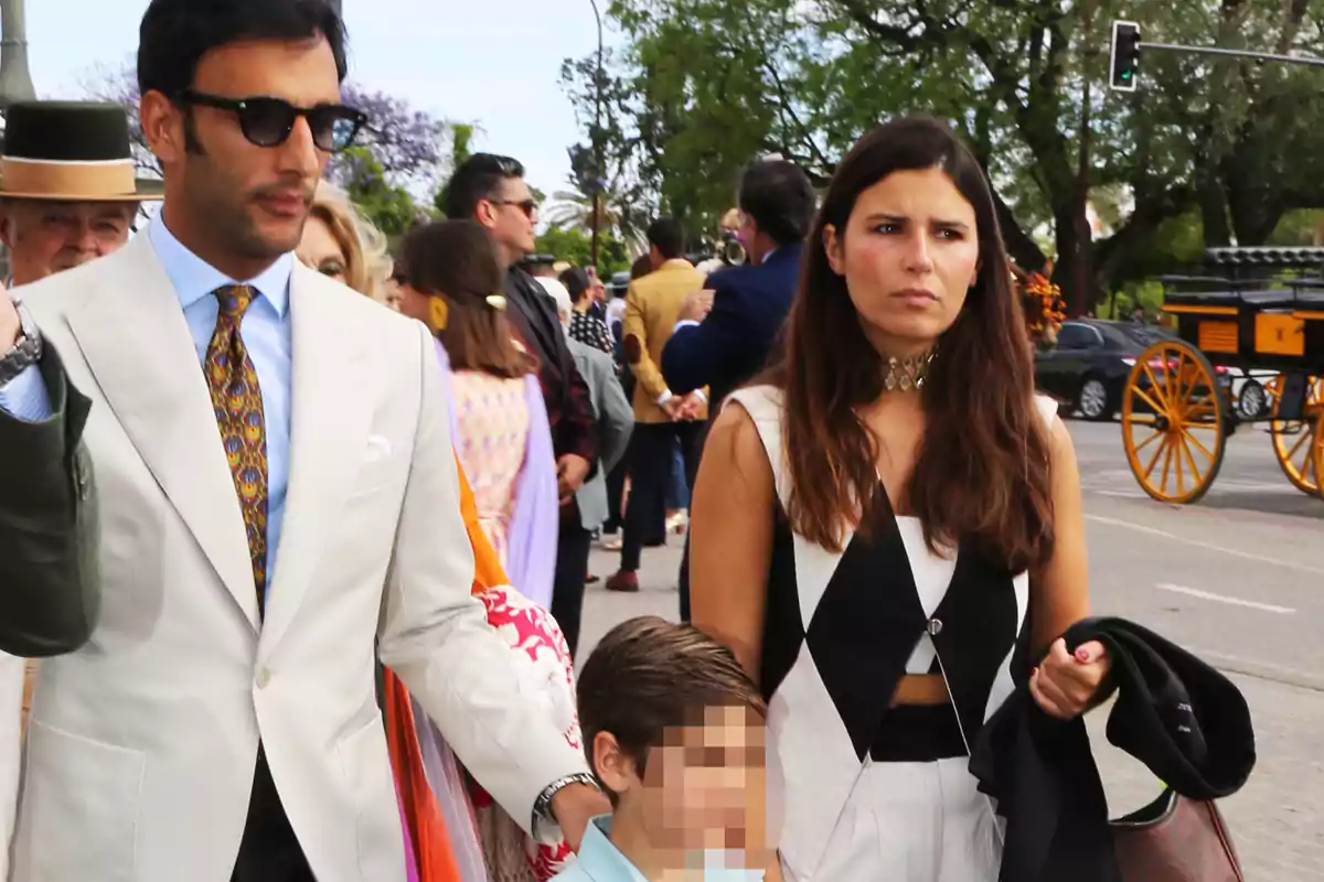 Un grupo de personas bien vestidas camina por una calle concurrida, con un carruaje al fondo. Un grupo de personas bien vestidas camina por una calle concurrida, con un carruaje al fondo.