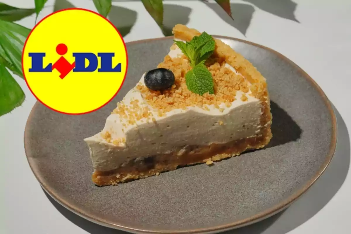 Una porción de pastel con una base crujiente y una capa cremosa, decorada con una hoja de menta y una baya, se presenta en un plato gris junto a un logotipo de supermercado. Una porción de pastel con una base crujiente y una capa cremosa, decorada con una hoja de menta y una baya, se presenta en un plato gris junto a un logotipo de supermercado.