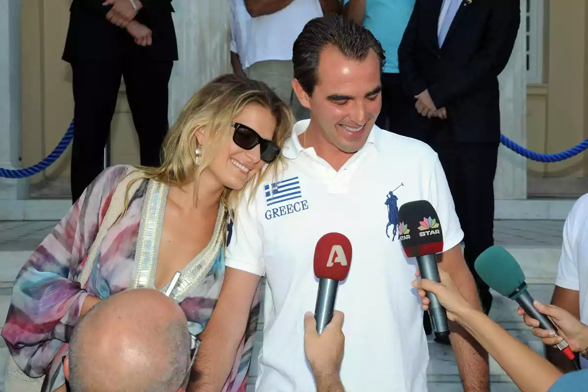 Tatiana Blatnik y Nicolás de Grecia sonriente es entrevistada por varios periodistas con micrófonos en un evento al aire libre. Tatiana Blatnik y Nicolás de Grecia sonriente es entrevistada por varios periodistas con micrófonos en un evento al aire libre.