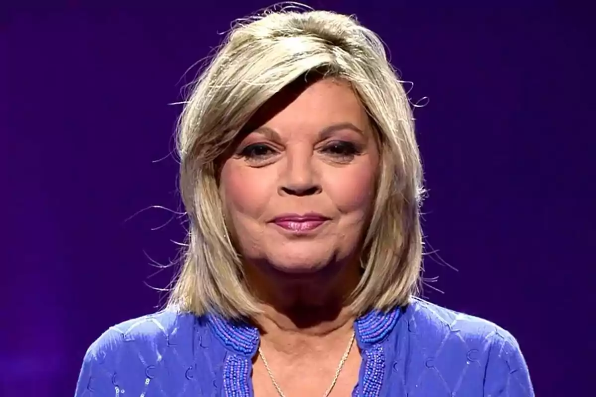 Terelu Campos con cabello rubio y expresión serena, vestida con una blusa azul, sobre un fondo morado en De Viernes. Terelu Campos con cabello rubio y expresión serena, vestida con una blusa azul, sobre un fondo morado en De Viernes.