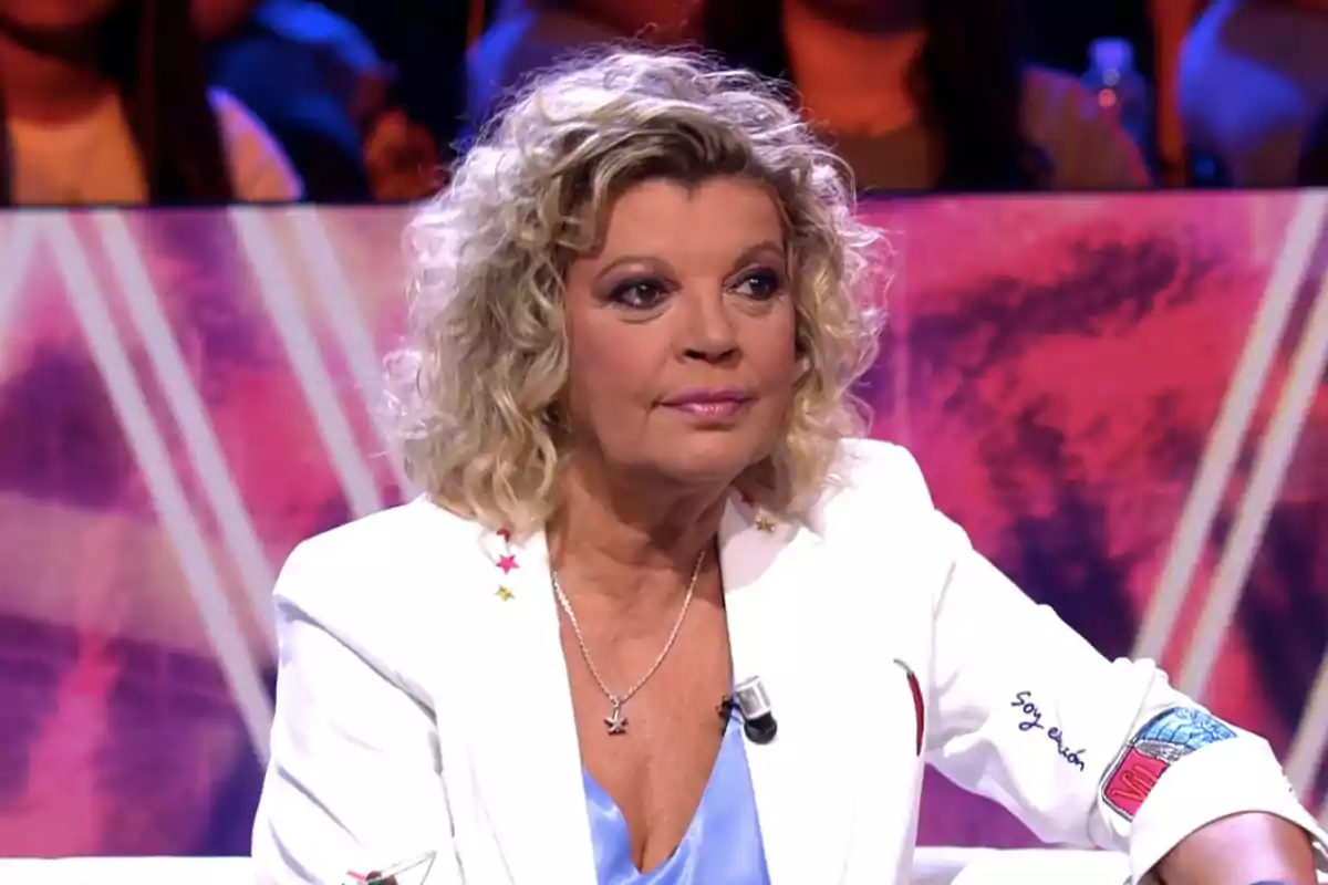 Terelu Campos con chaqueta blanca sentada en un plató de televisión con fondo colorido Terelu Campos con chaqueta blanca sentada en un plató de televisión con fondo colorido