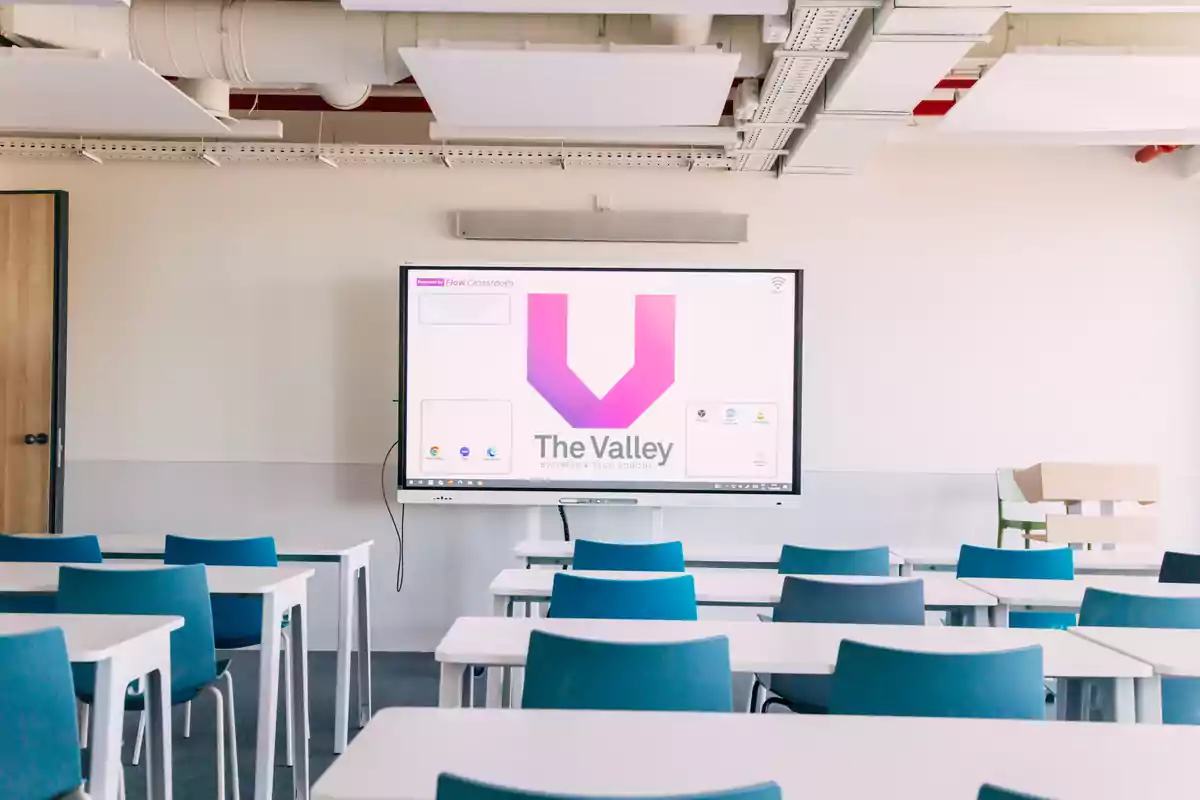 Modern classroom with blue chairs and white tables facing a large screen displaying "The Valley" logo.