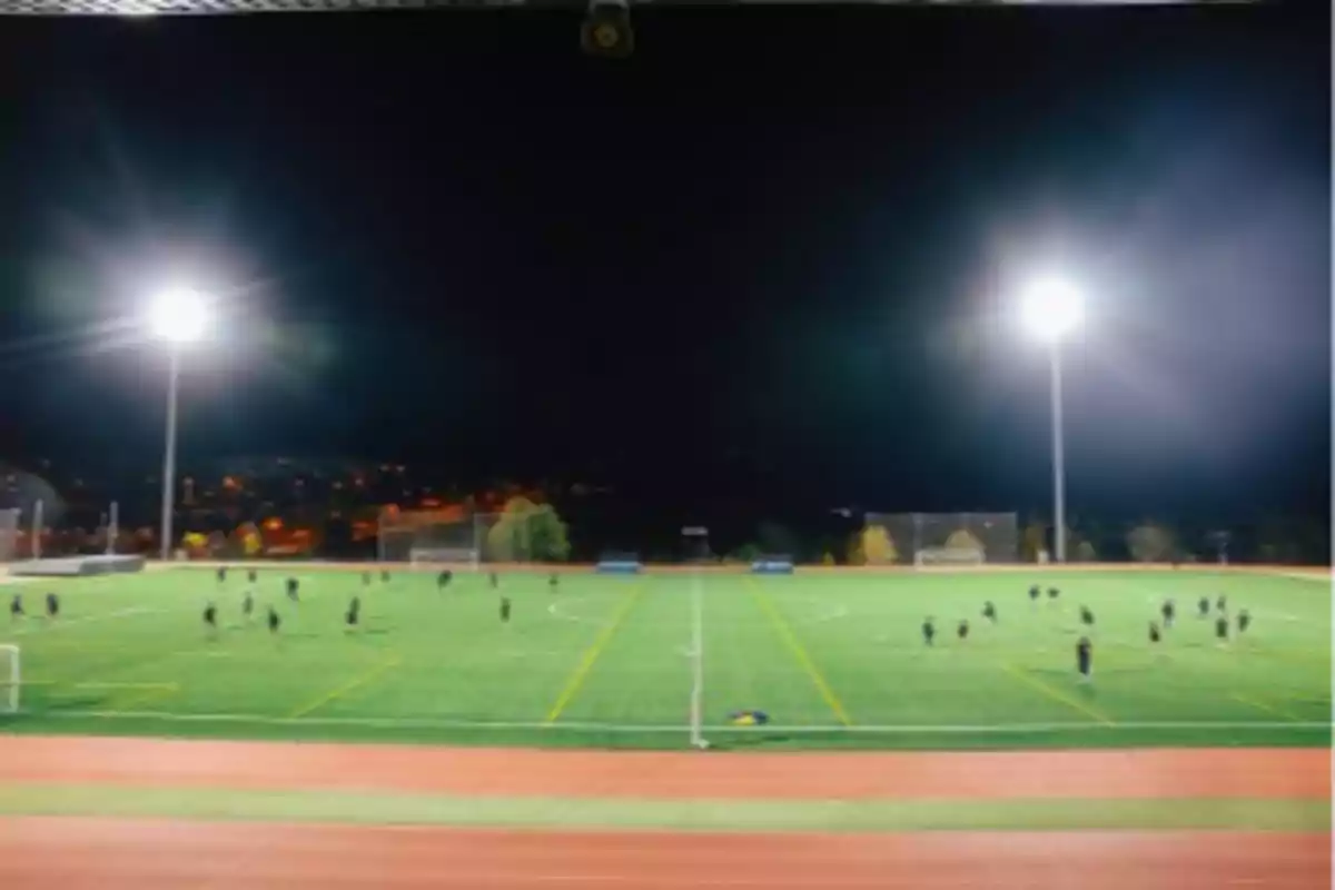 Campo de fútbol iluminado por la noche con personas jugando.