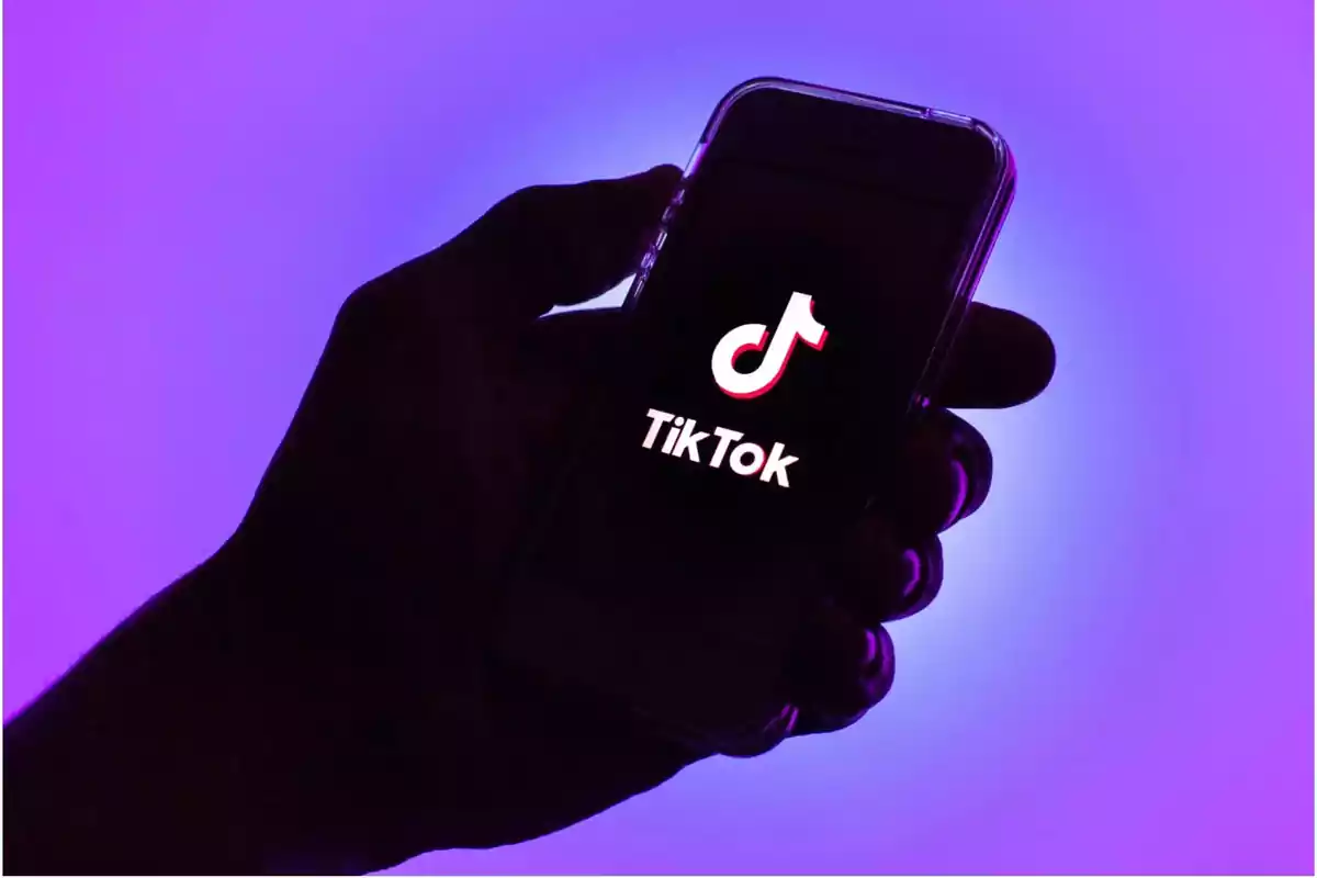 Una mano sostiene un teléfono móvil que muestra el logo de TikTok sobre un fondo morado. Una mano sostiene un teléfono móvil que muestra el logo de TikTok sobre un fondo morado.