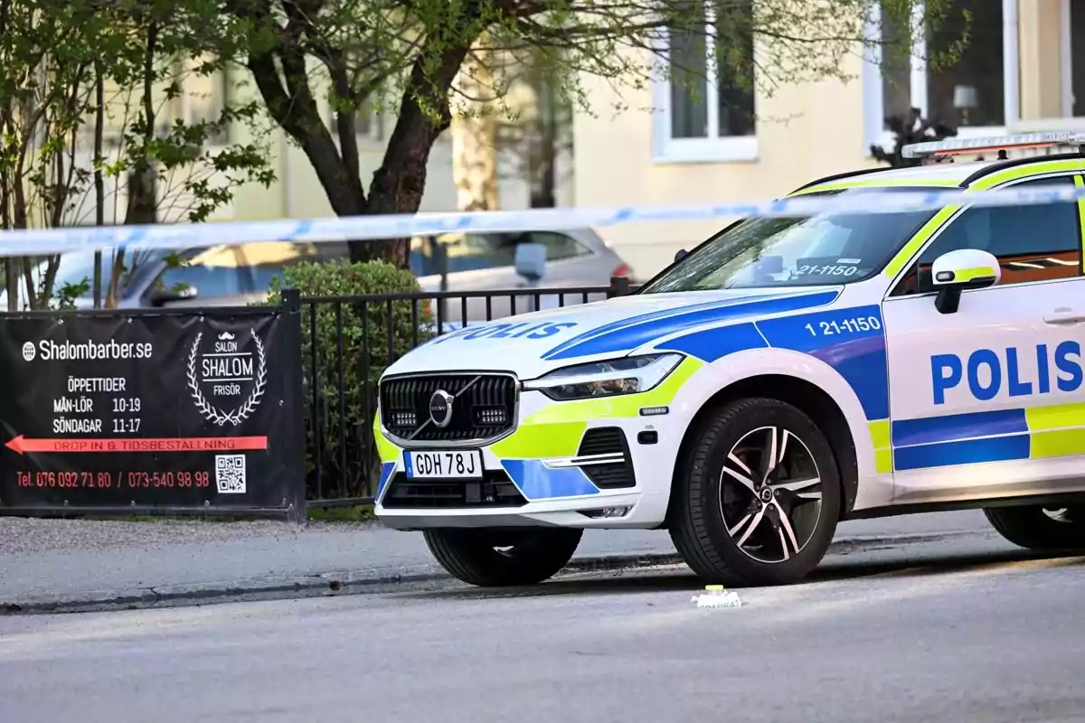 Un coche de policía estacionado junto a una valla con un cartel de una barbería en un entorno urbano. Un coche de policía estacionado junto a una valla con un cartel de una barbería en un entorno urbano.