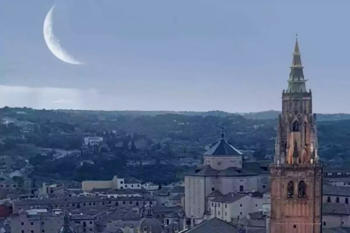 Vista panorámica de una ciudad con una iglesia y una luna creciente en el cielo.