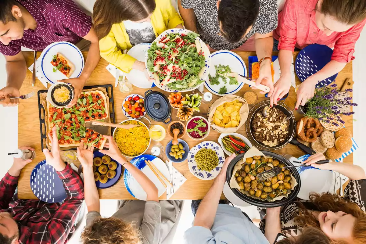 Un grupo de personas compartiendo una comida variada en una mesa llena de platos coloridos y diferentes tipos de alimentos.