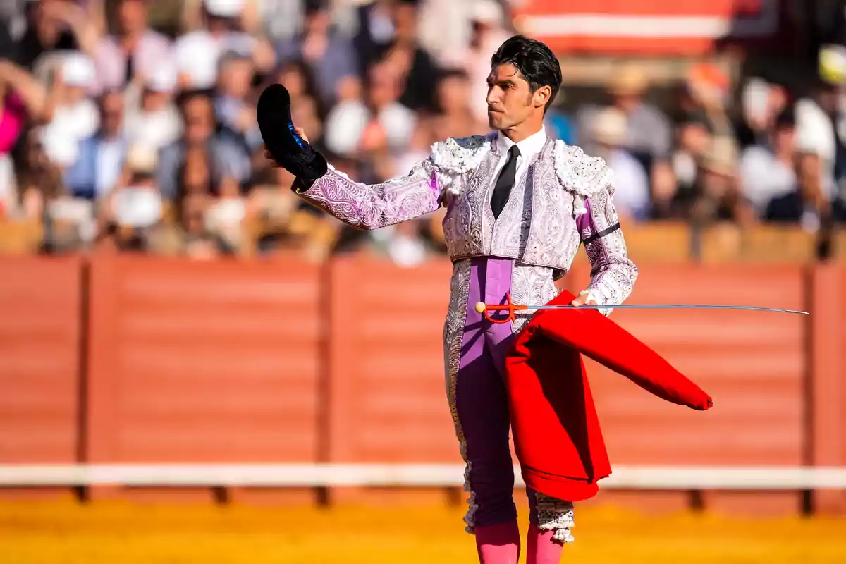 Un torero en la plaza sosteniendo su montera y capote mientras el público observa. Un torero en la plaza sosteniendo su montera y capote mientras el público observa.