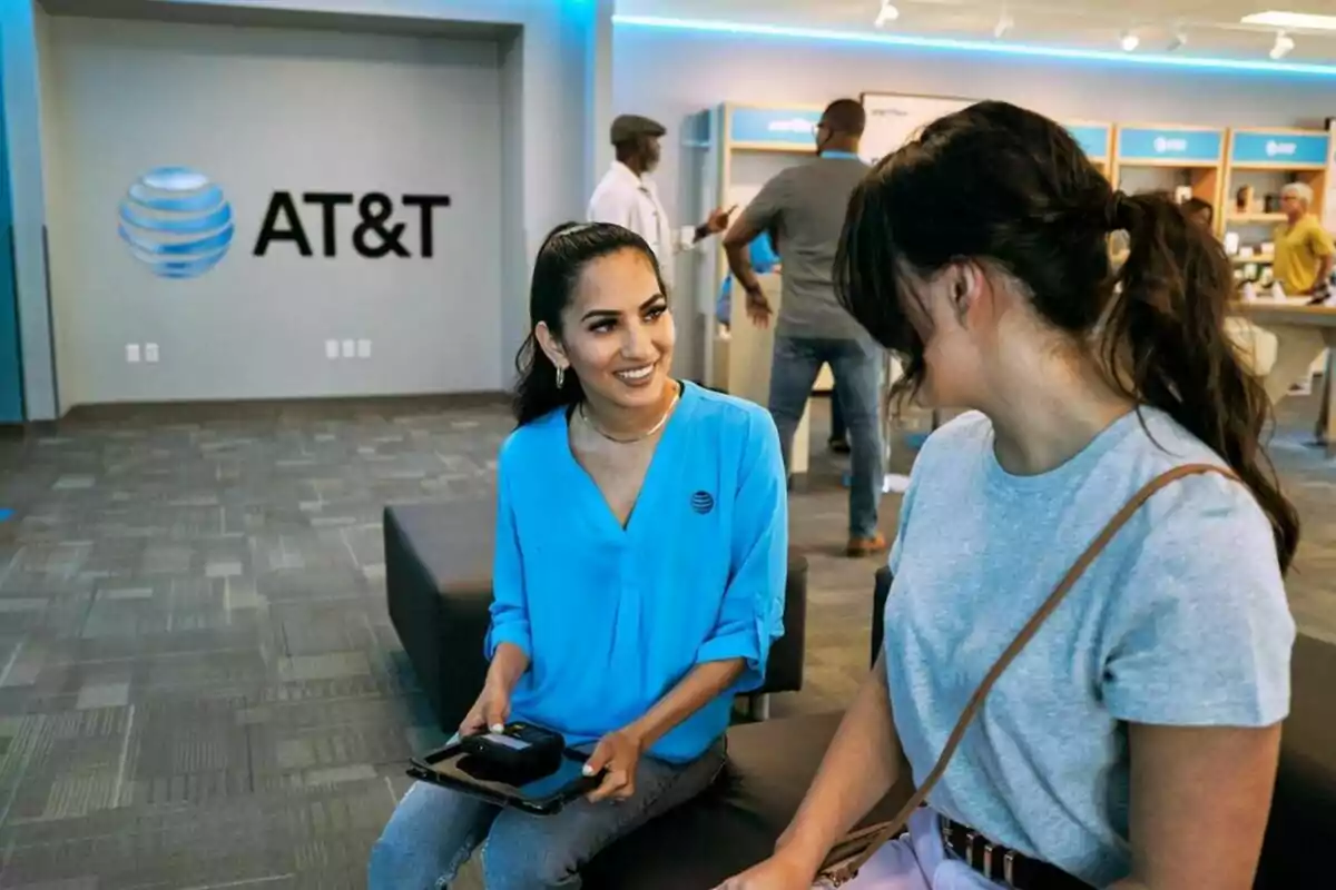Dos personas conversan en una tienda de AT&T, una de ellas lleva un uniforme azul y sostiene una tableta. Dos personas conversan en una tienda de AT&T, una de ellas lleva un uniforme azul y sostiene una tableta.