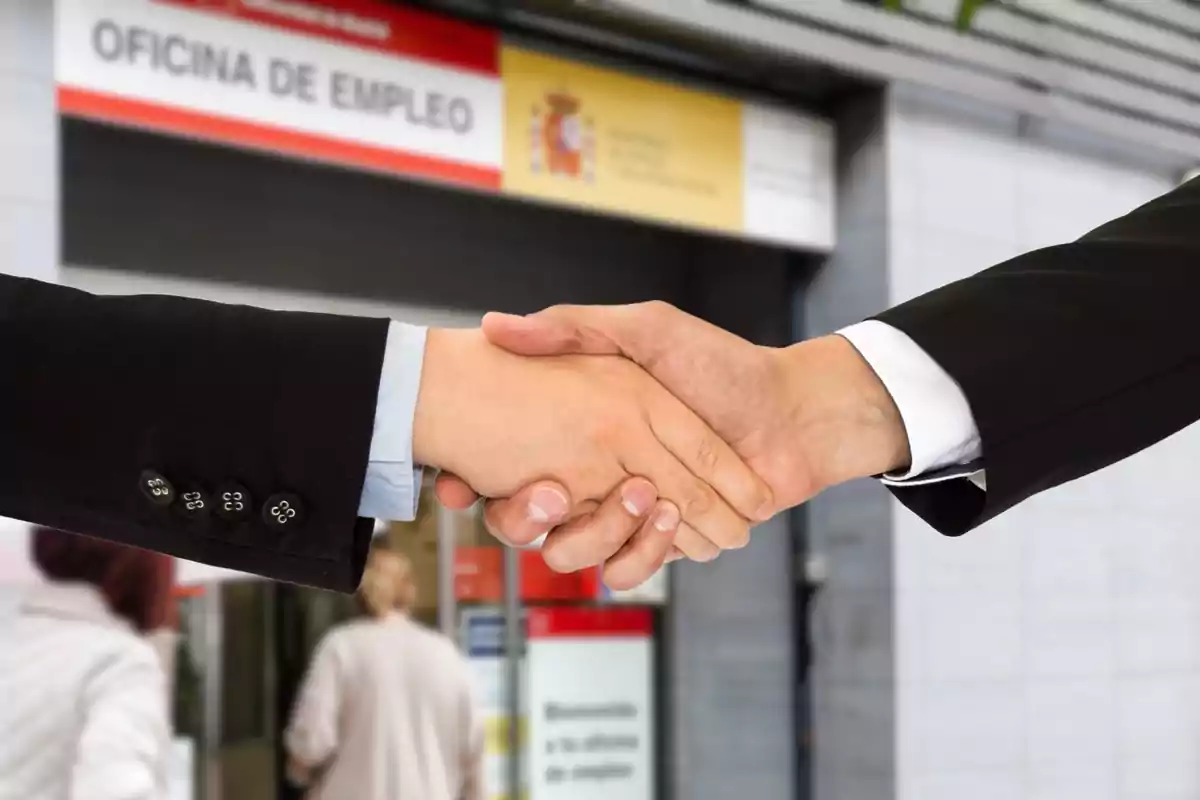 Dos personas estrechándose la mano frente a una oficina de empleo.