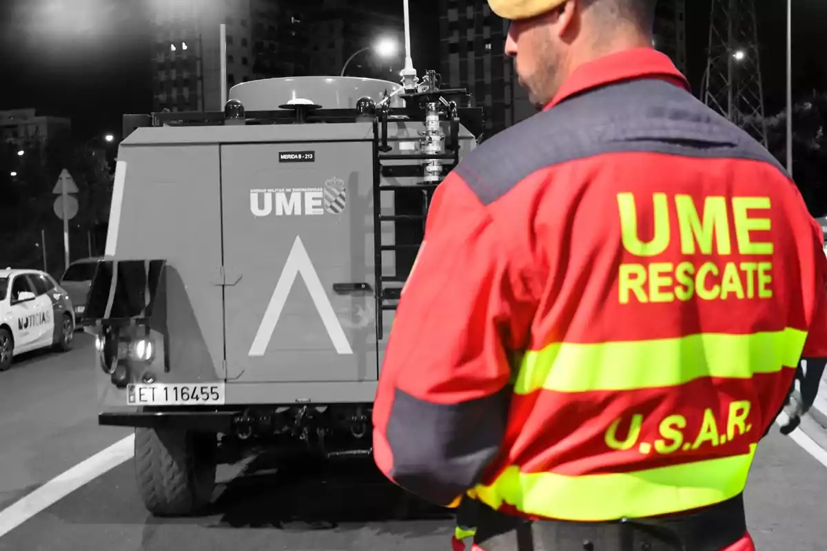Un miembro de la Unidad Militar de Emergencias (UME) con un uniforme de rescate observa un vehículo de la UME en una calle durante la noche.